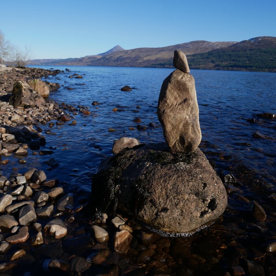 Stones stacked along Loch Rannoch with Schiehallion mountain in the distance